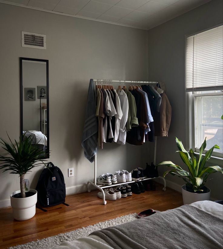 a bedroom with clothes hanging on a rack and a potted plant in the corner