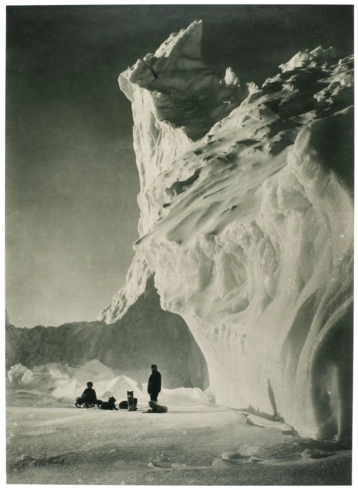 some people are standing in the snow near an iceberg