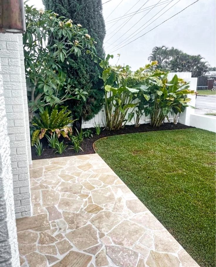 an outdoor area with grass and plants in the back yard, next to a white fence