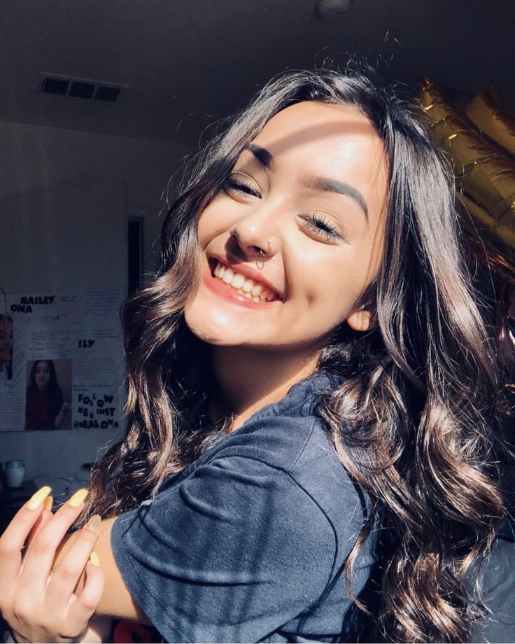 a woman with long hair smiling and holding her arms around her neck while looking at the camera