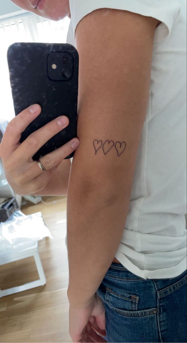 a woman holding a cell phone with two hearts tattooed on the back of her arm