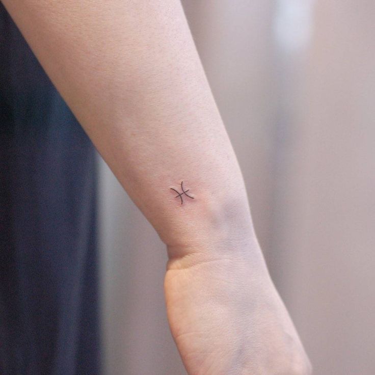 a small cross tattoo on the left inner wrist is shown in this image, it appears to be an arrow