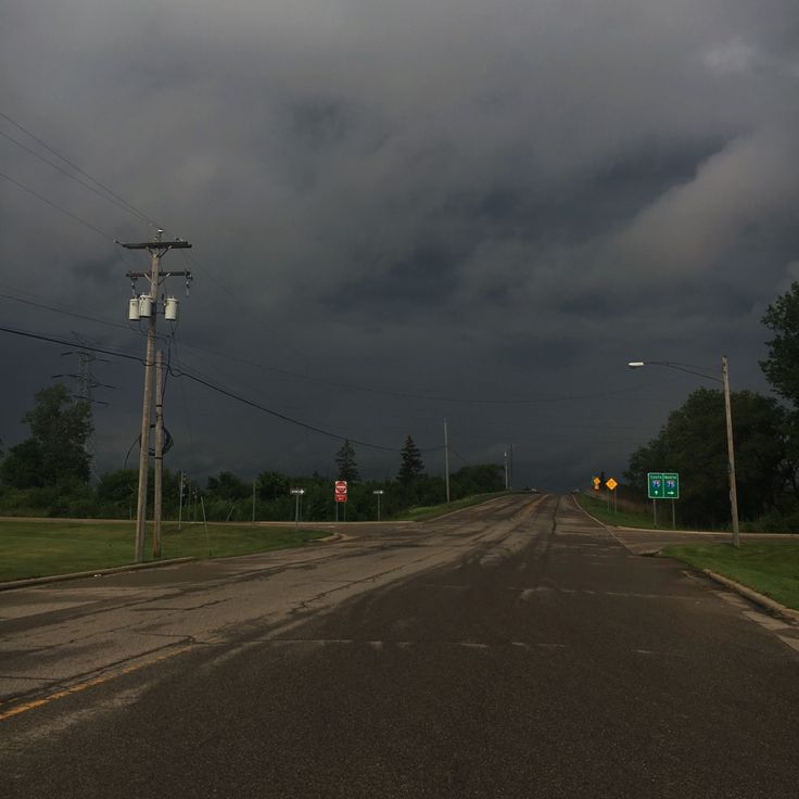 an empty road with storm clouds in the background and street signs on either side,