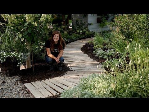 a woman kneeling down on a wooden walkway surrounded by trees and plants in the garden