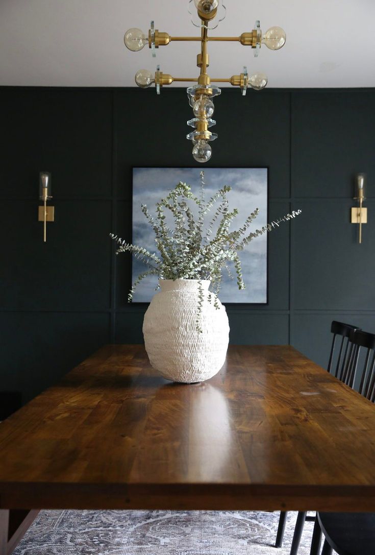 a dining room table with a white vase on it and a painting hanging above the table