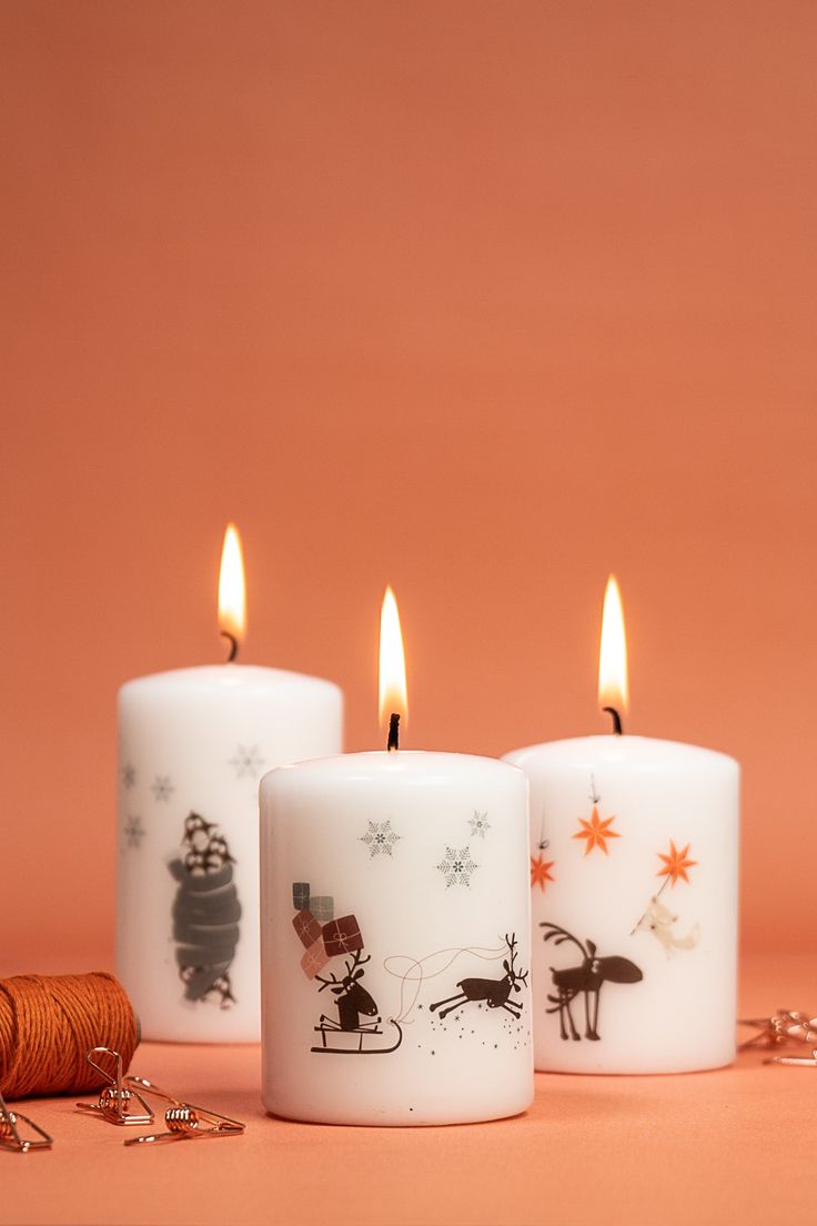 three white candles with christmas designs on them