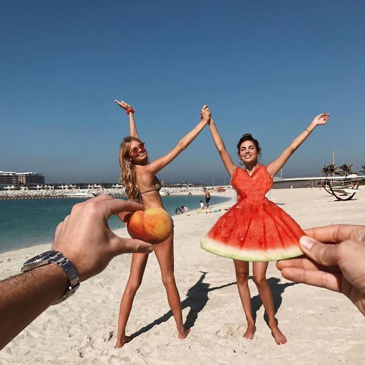 two girls are standing on the beach with their arms in the air and one girl is wearing a watermelon dress