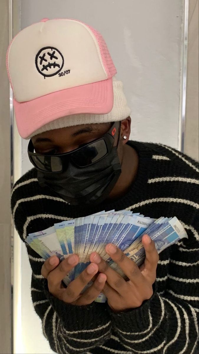 a person wearing a face mask and holding money in their hands while wearing a hat