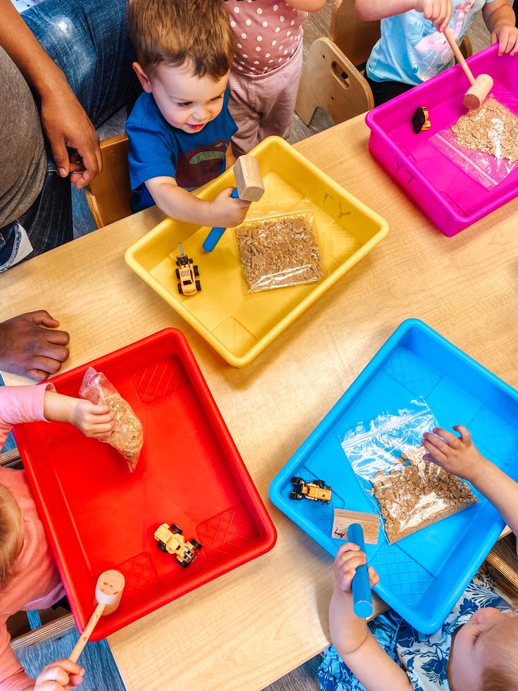 several children are sitting at a table and playing with different colored trays that have food on them