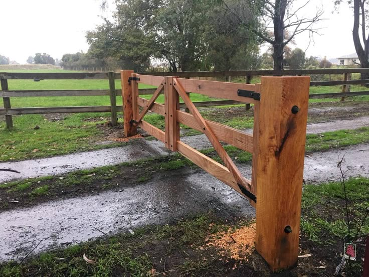 a wooden fence in the middle of a field with grass and trees behind it on a rainy day