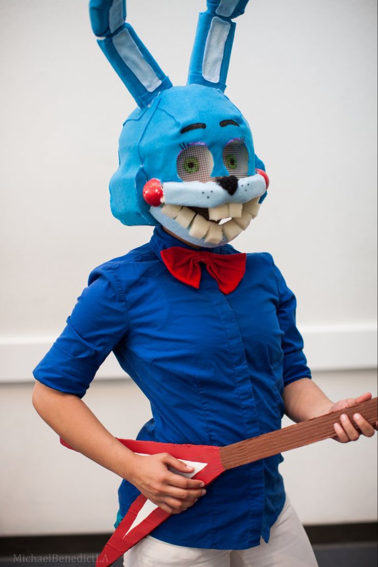 a woman wearing a blue bunny mask and holding a red ribbon around her waist while standing in front of a white wall