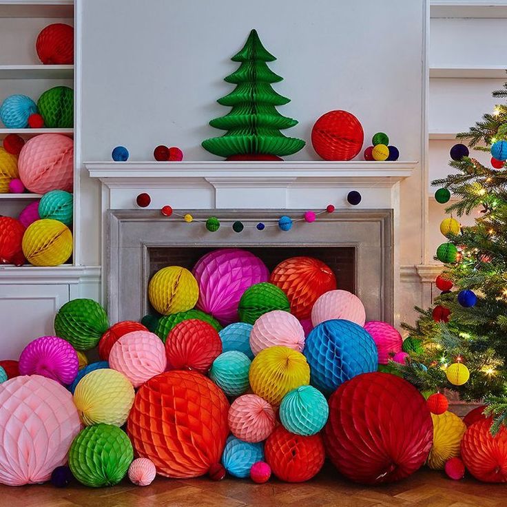 brightly colored paper balls surround a fireplace and christmas tree