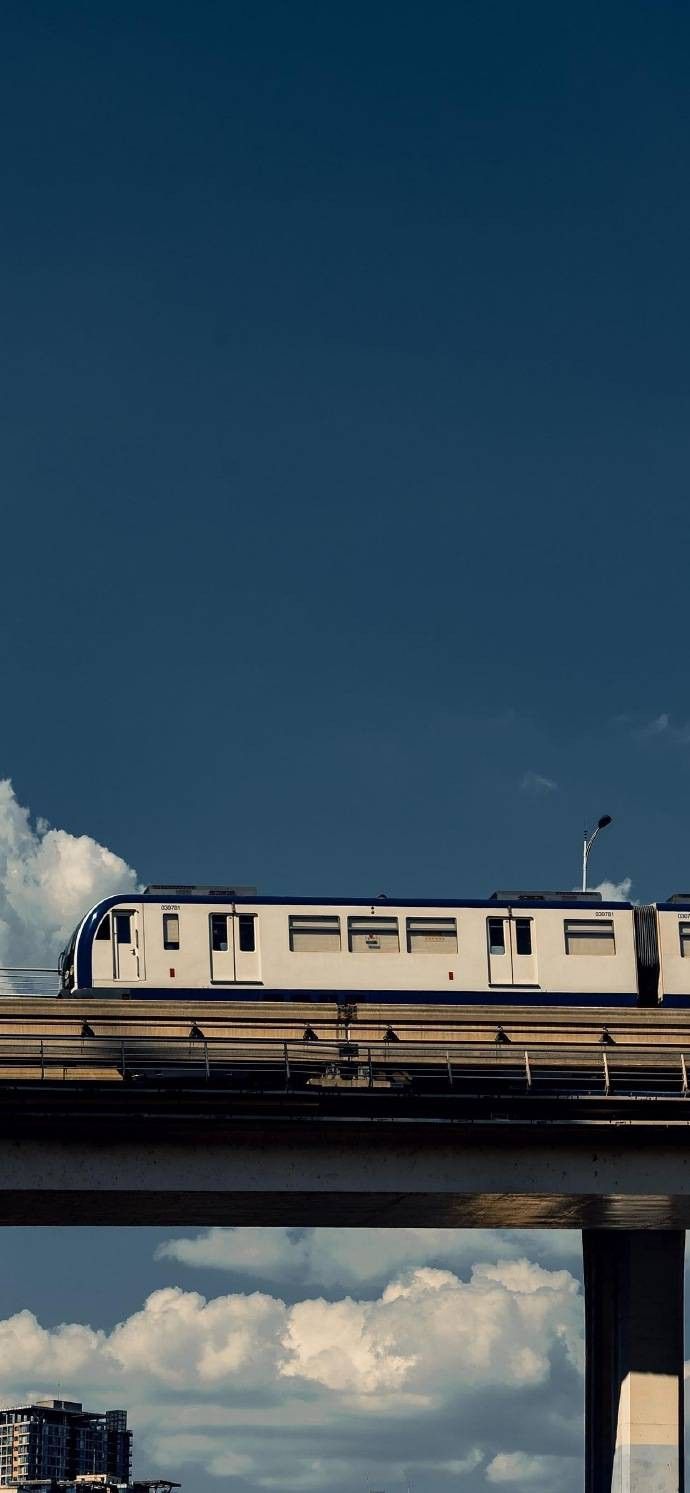 a passenger train traveling over a bridge in the middle of the day with blue sky and clouds behind it