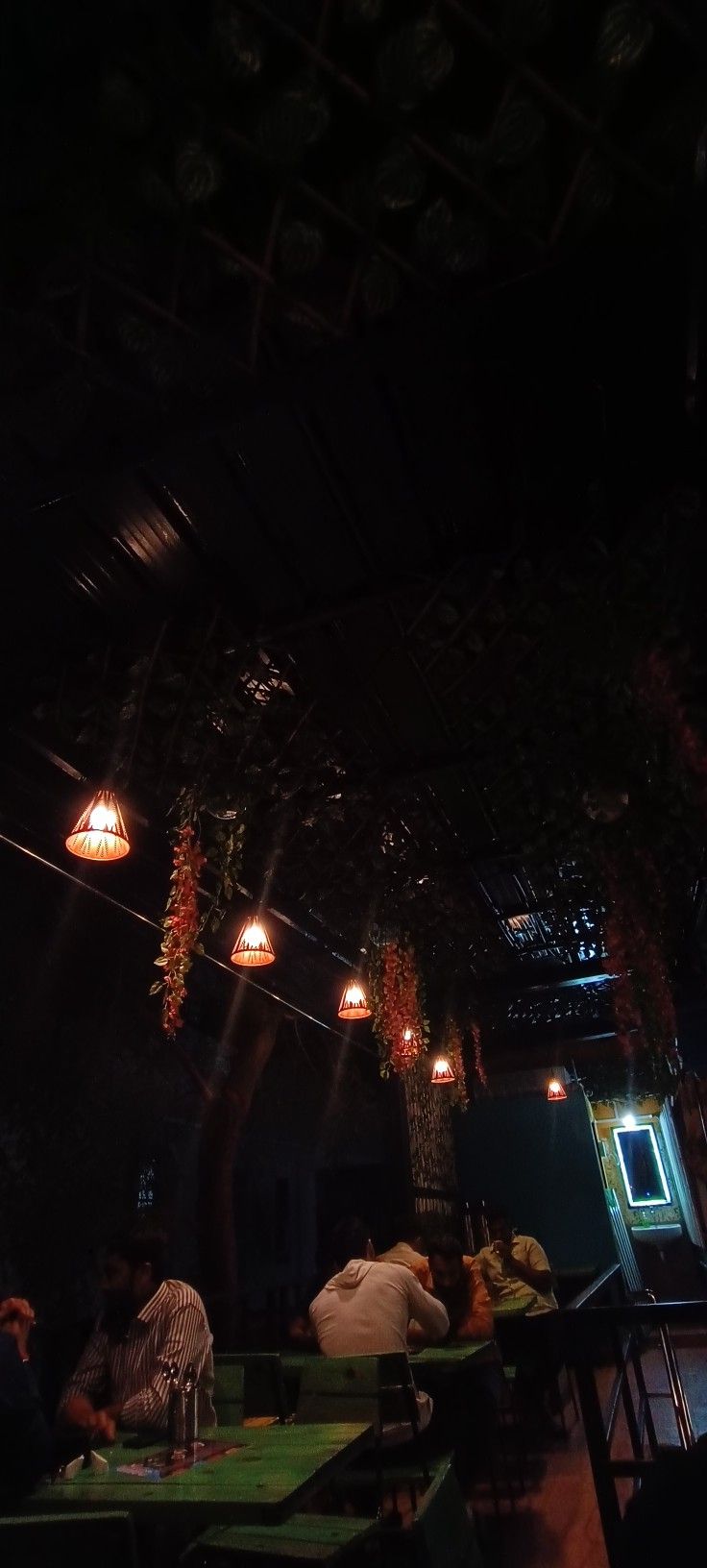 people sitting at tables in a dark room with lights hanging from the ceiling above them