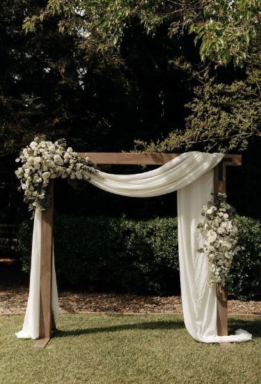 an outdoor wedding setup with white flowers and draping on the top of it