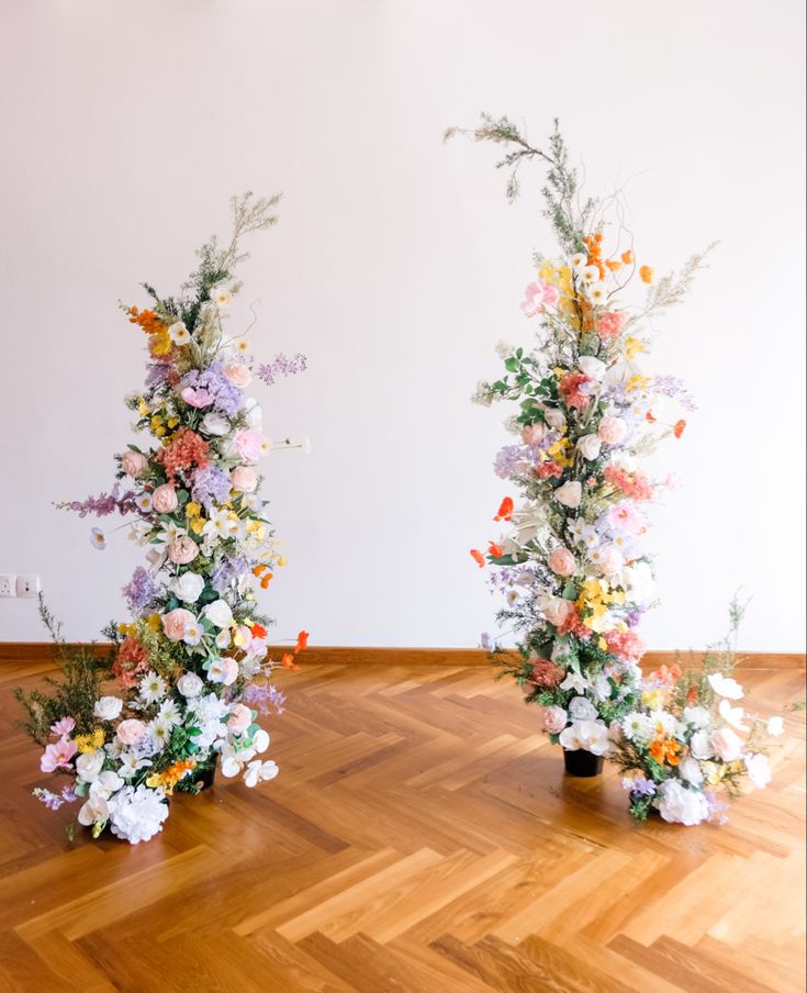 two tall vases filled with flowers on top of a wooden floor