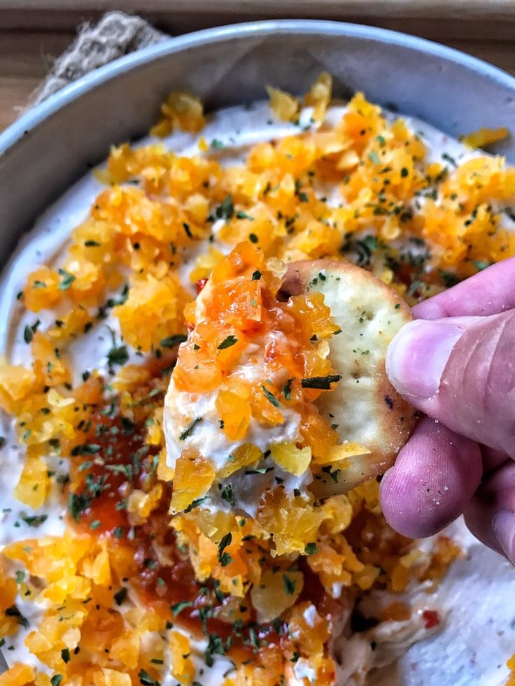 a hand is picking up some food from a bowl with sour cream and oranges