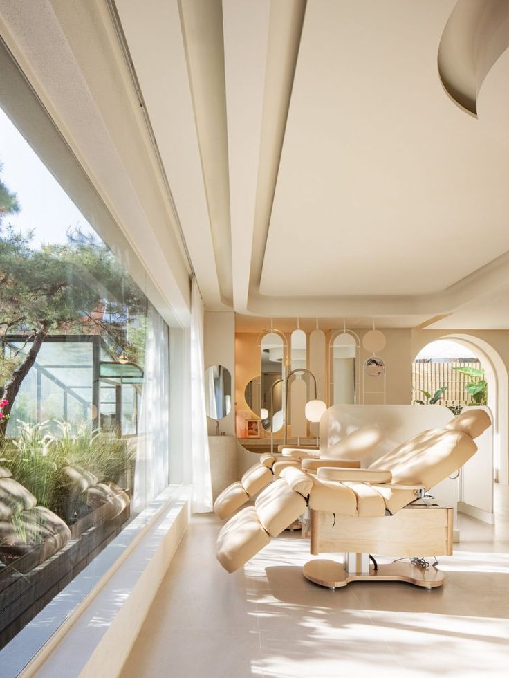 a living room filled with furniture next to a large glass window covered in plants and trees