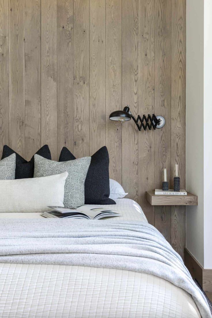 a bedroom with wood paneled walls and white bedding, along with black and grey pillows