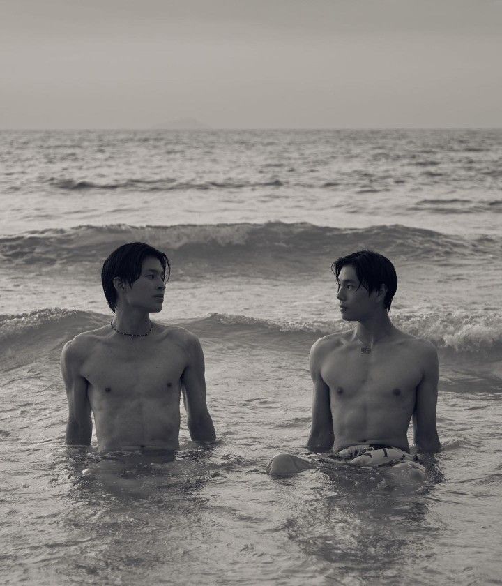 two young men sitting in the water at the edge of the ocean, facing each other