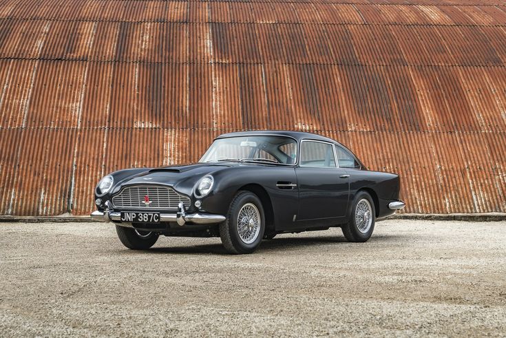 an old black sports car parked in front of a rusted metal wall and building