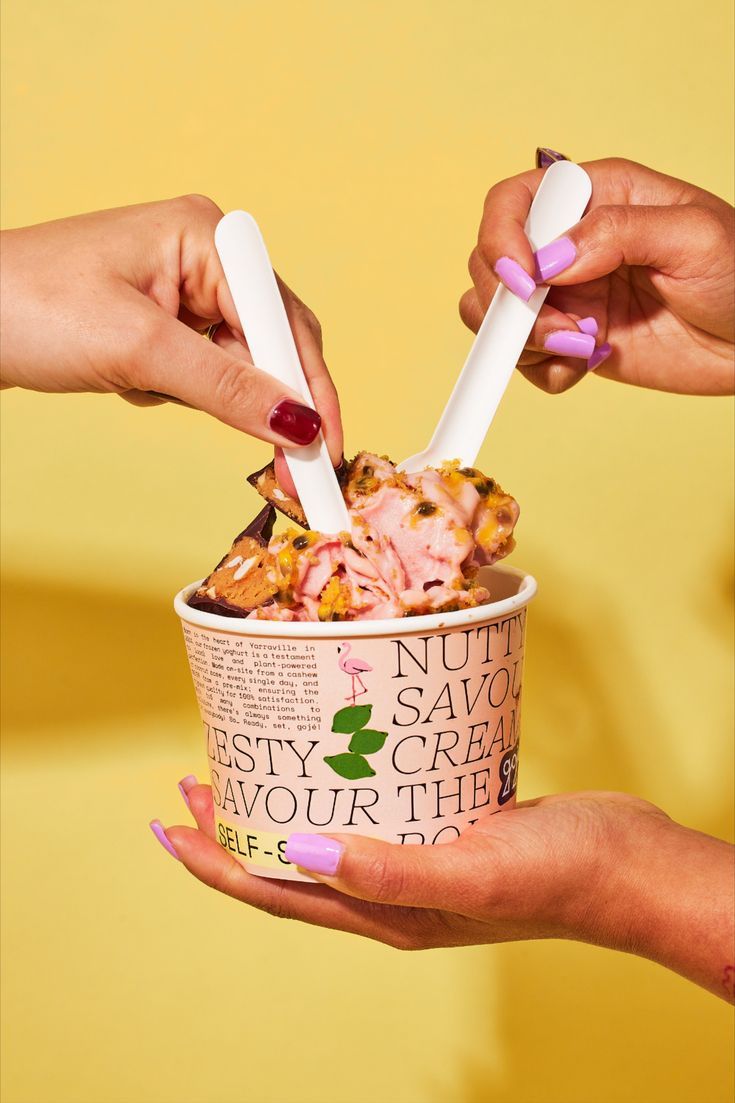 two hands holding ice cream cups with toppings in them