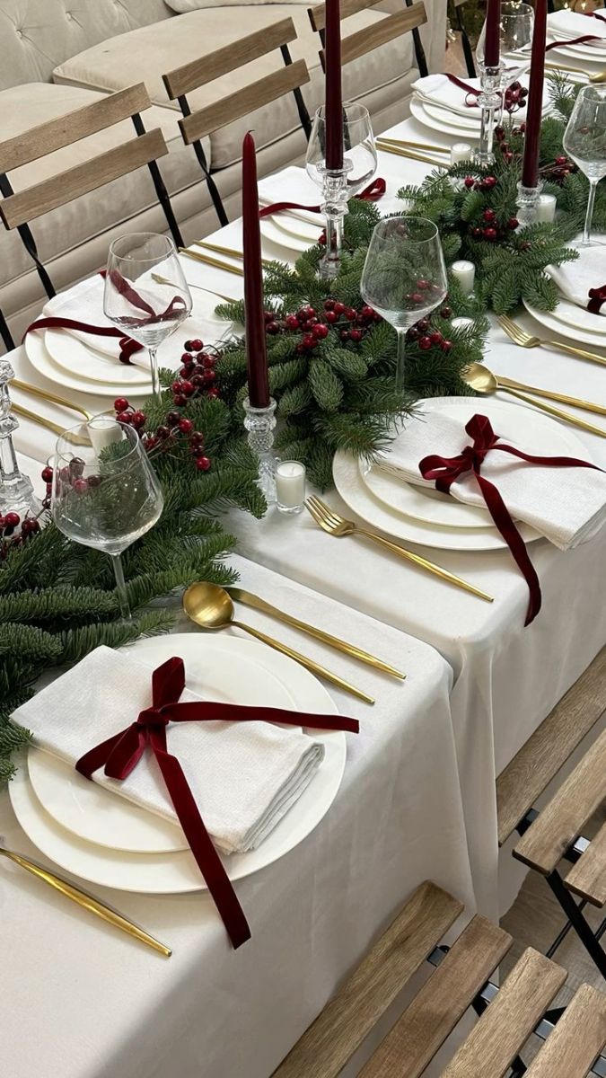 the table is set with white plates, silverware and greenery for christmas dinner