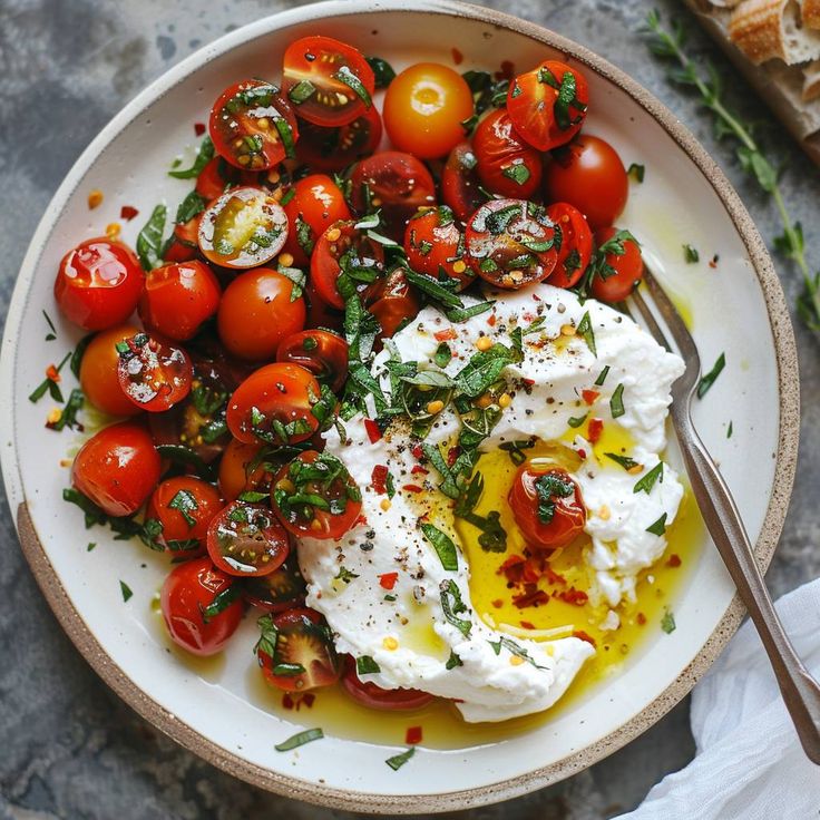 a white bowl filled with tomatoes and sour cream on top of a table next to bread