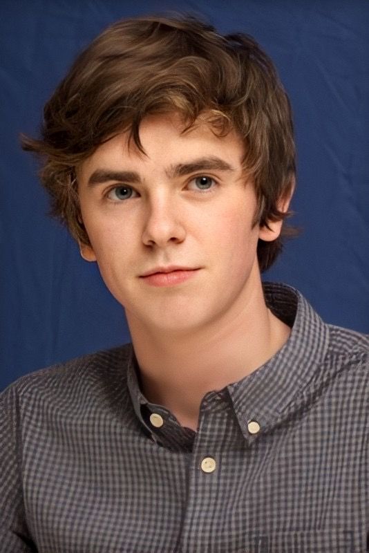 a young man is posing for a photo in front of a blue background wearing a button up shirt