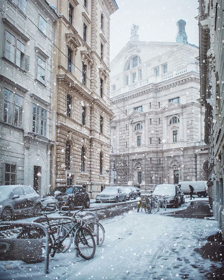 a snowy city street filled with lots of parked cars and bicycles next to tall buildings