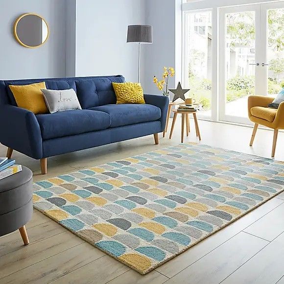 a living room with blue couches and yellow pillows on the rugs in front of windows