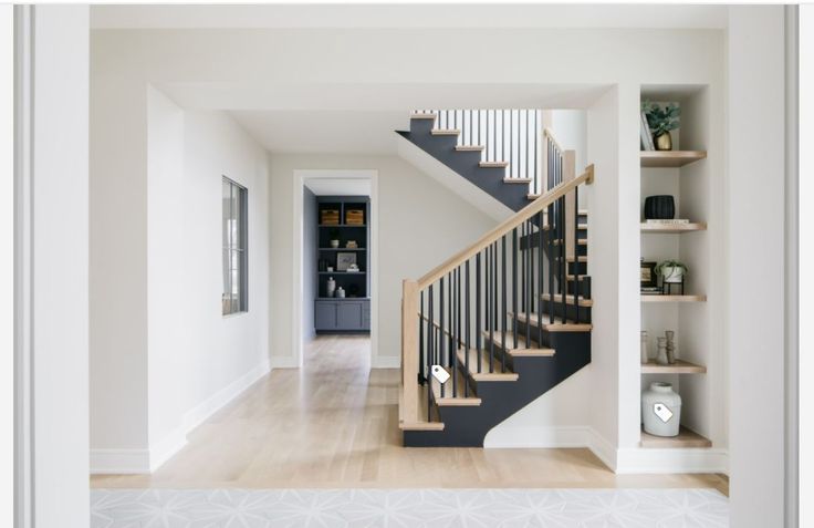 a staircase in a house with white walls and wood flooring, along with open shelving