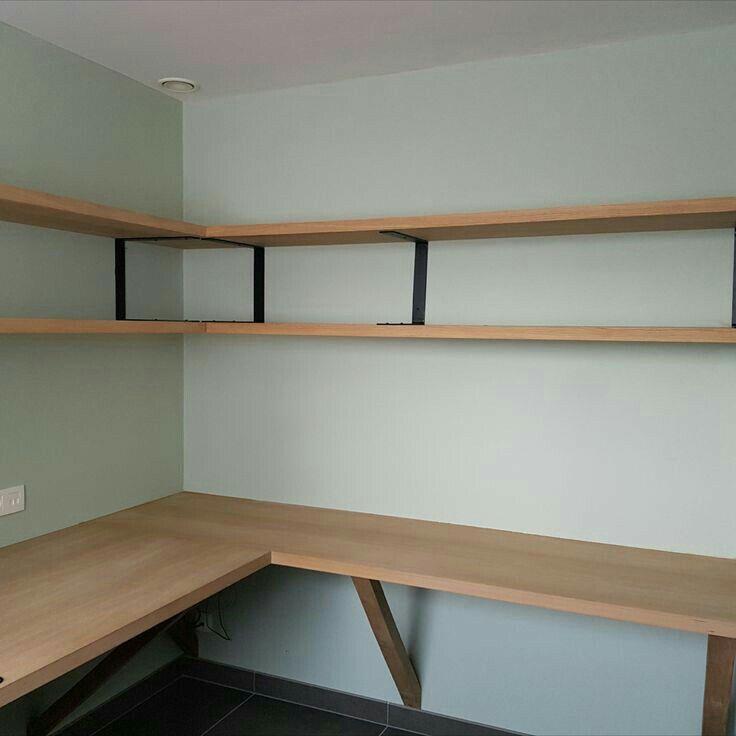 an empty corner desk with shelves on the wall