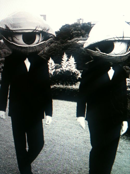 two men in suits walking down the street with large eyes on their heads and one wearing a top hat