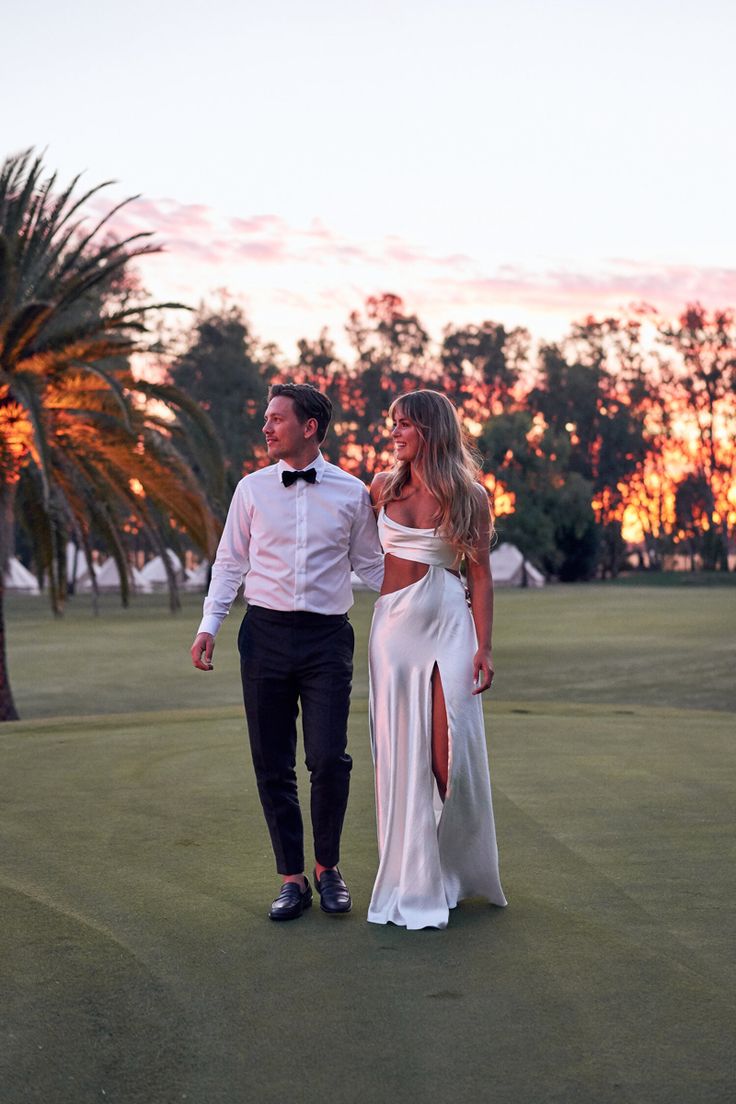 a man and woman walking on a golf course at sunset with palm trees in the background