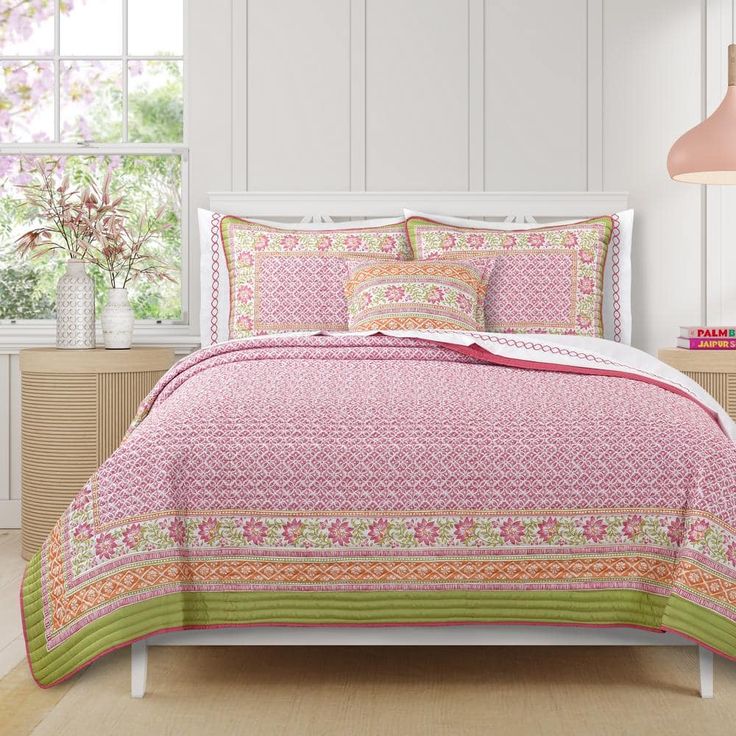 a bed with pink and green bedspread in a room next to a window