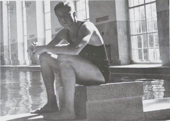 black and white photograph of a man sitting on steps next to a pool with his legs crossed