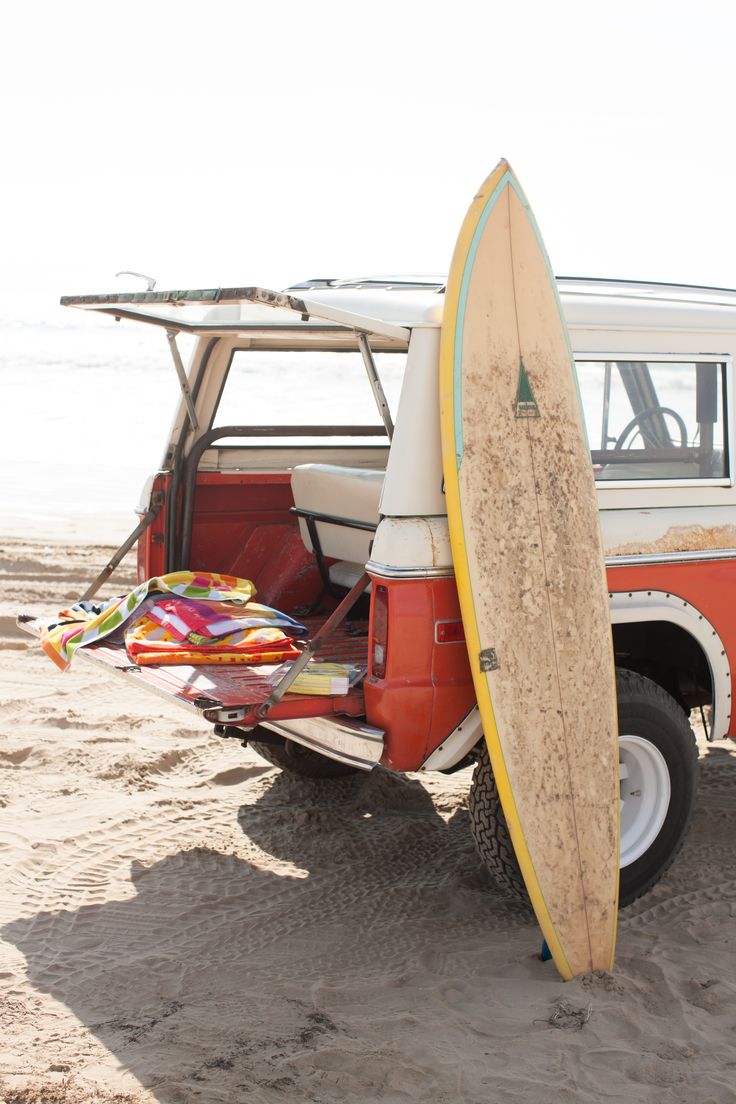 the surfboard is propped up against the vehicle on the beach