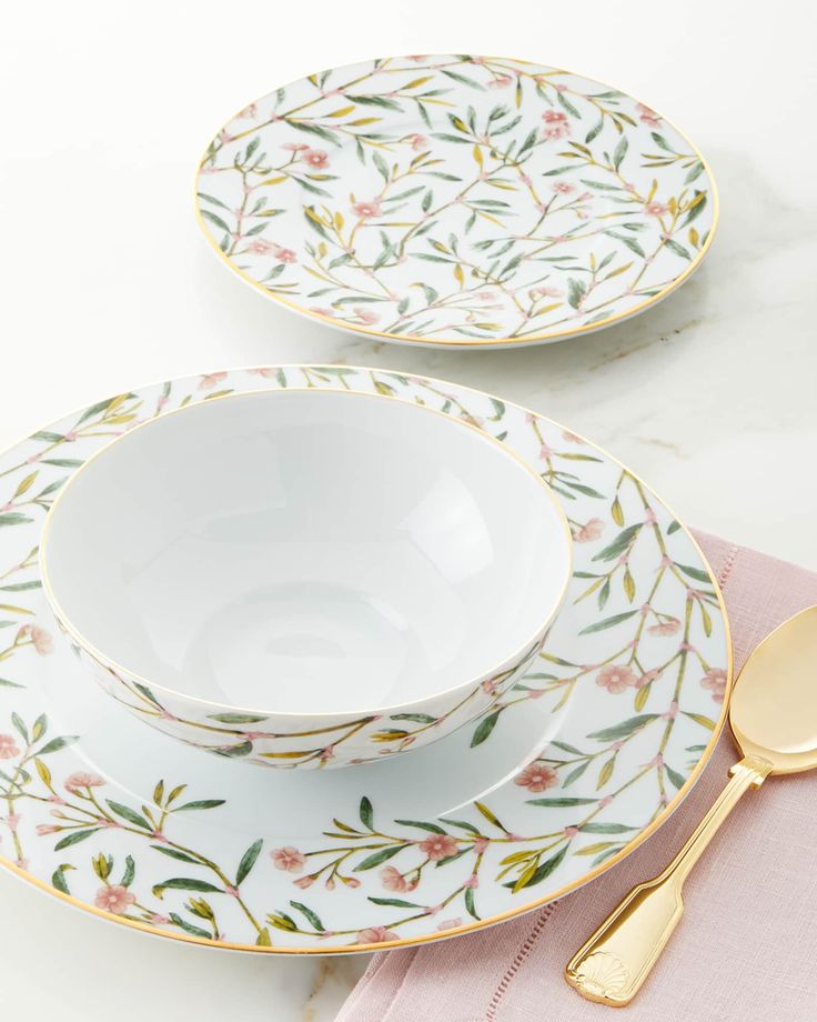 two plates with gold spoons on them sitting next to each other near a pink napkin