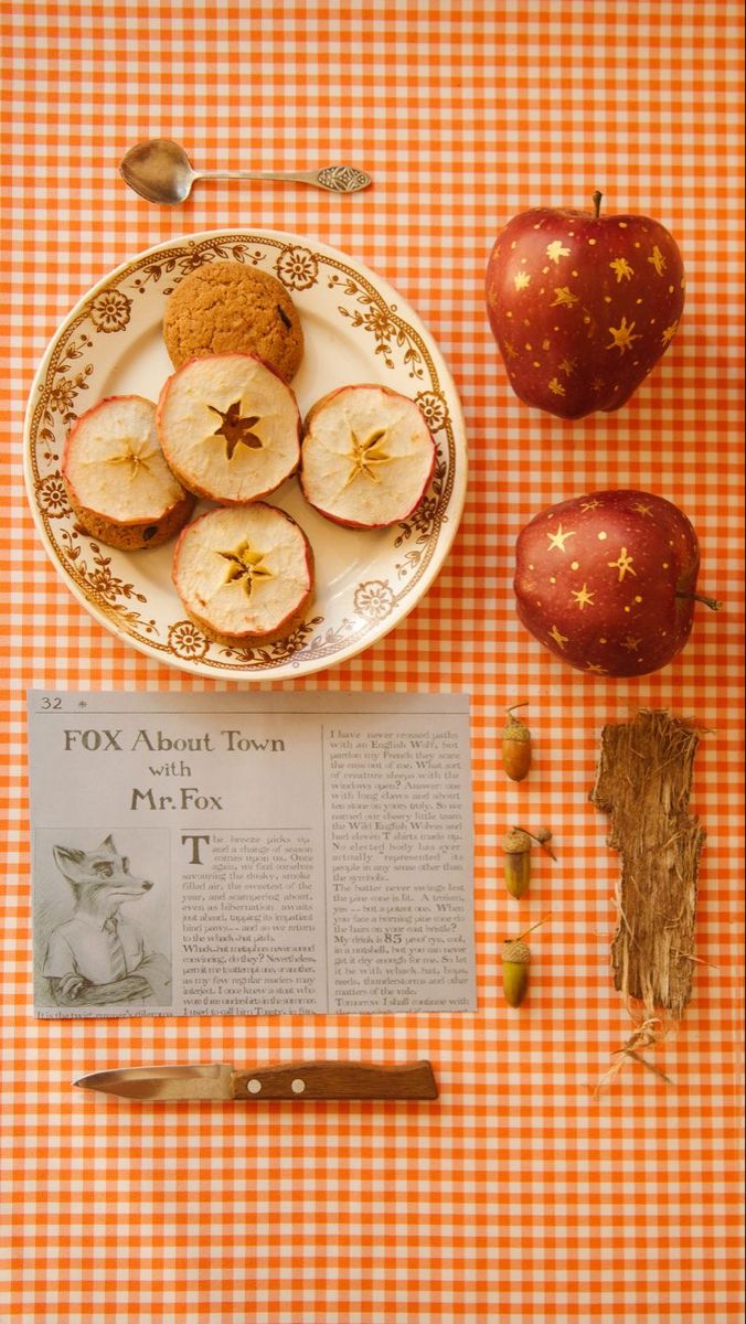 apples and other food on a table with an orange checkered tablecloth next to it