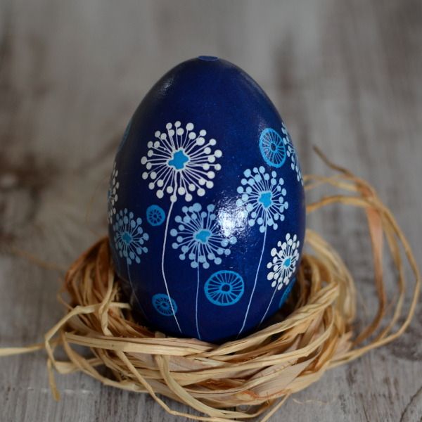 an egg painted with blue and white flowers sits in a nest on a wooden surface