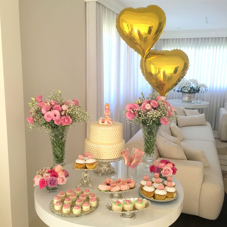 a table topped with cupcakes and cake next to vases filled with flowers