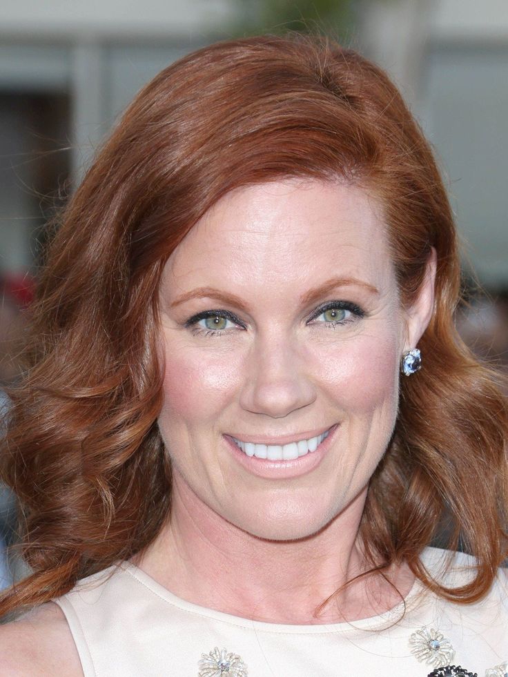 a woman with red hair and blue eyes smiling in front of the camera, wearing a white dress