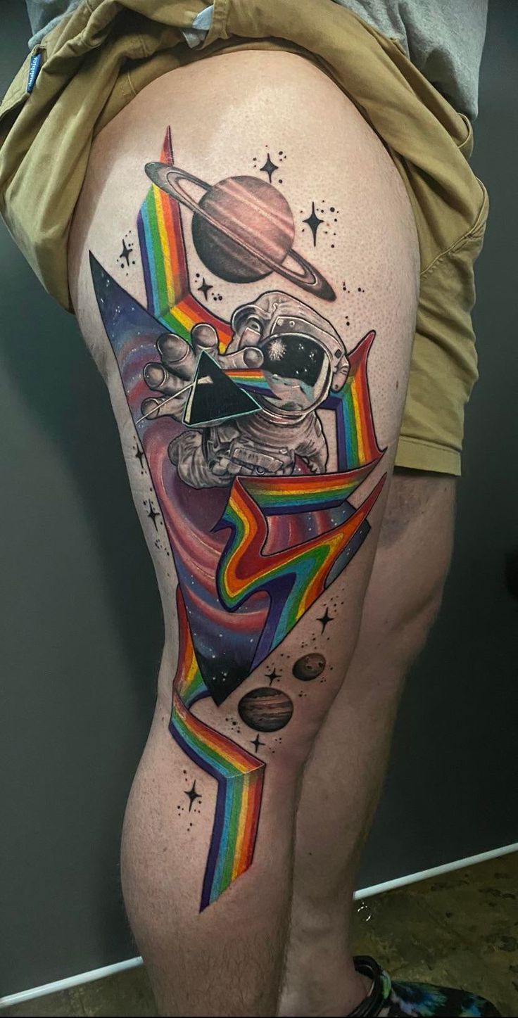 a man's thigh with an astronaut tattoo on it and planets in the background