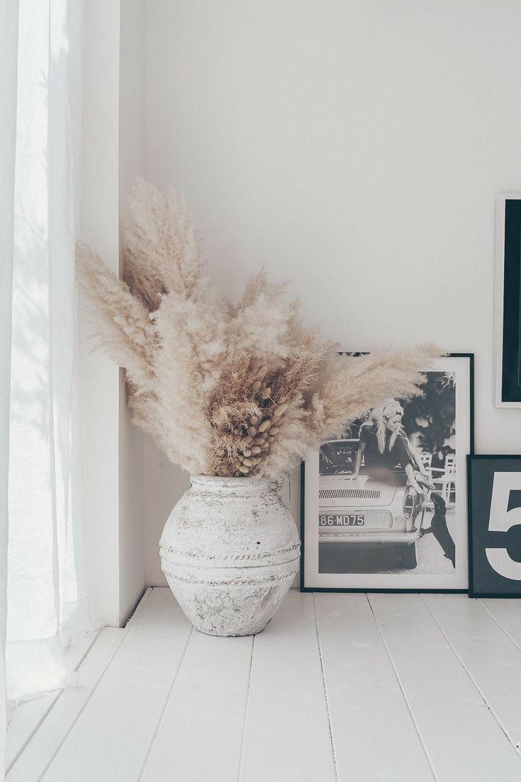 a white vase filled with dry grass next to pictures