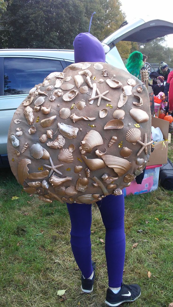 a person is standing in the grass with a large rock shaped like a sea shell