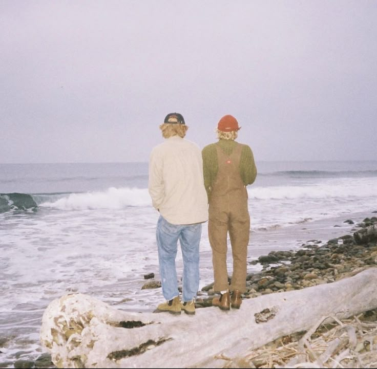 two men standing on rocks near the ocean