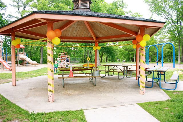 a wooden gazebo in a park with picnic tables and play equipment on the ground