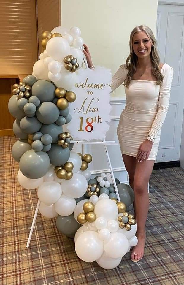 a woman standing next to a sign that says welcome home on it and balloons all around her