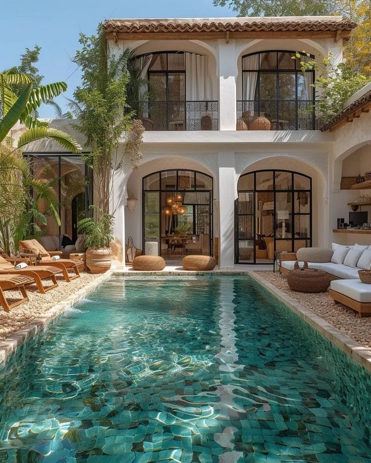 an outdoor swimming pool with lounge chairs around it and a house in the back ground